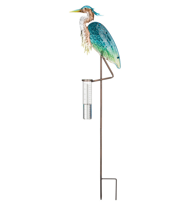a decorative sculpted heron holding a rain collection tube with gauges for measuring rainfall extending from one of its legs atop a staff against a white background