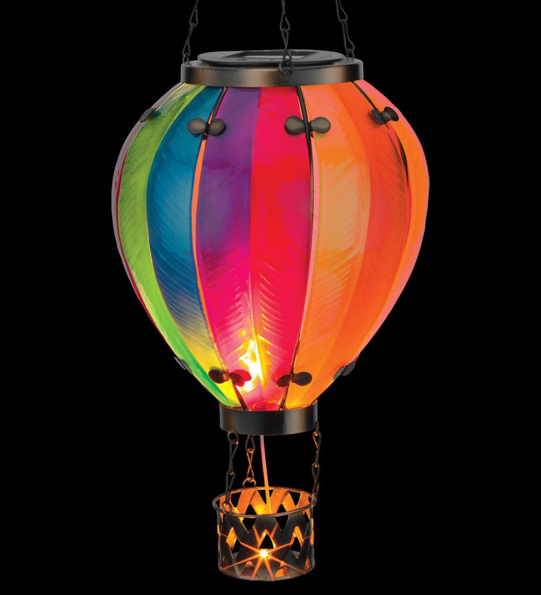 Close up of a colorful hot air balloon-shaped solar light with a metal basket, isolated on a black background.