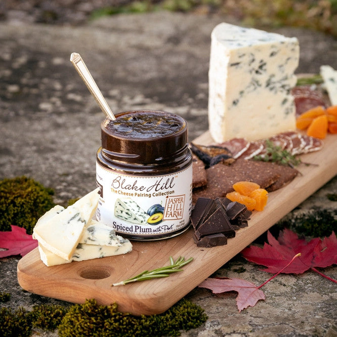 a cutting board with a spread of snacks including cheese, crackers, fruit, and the Spiced Plum with Port preserves jar