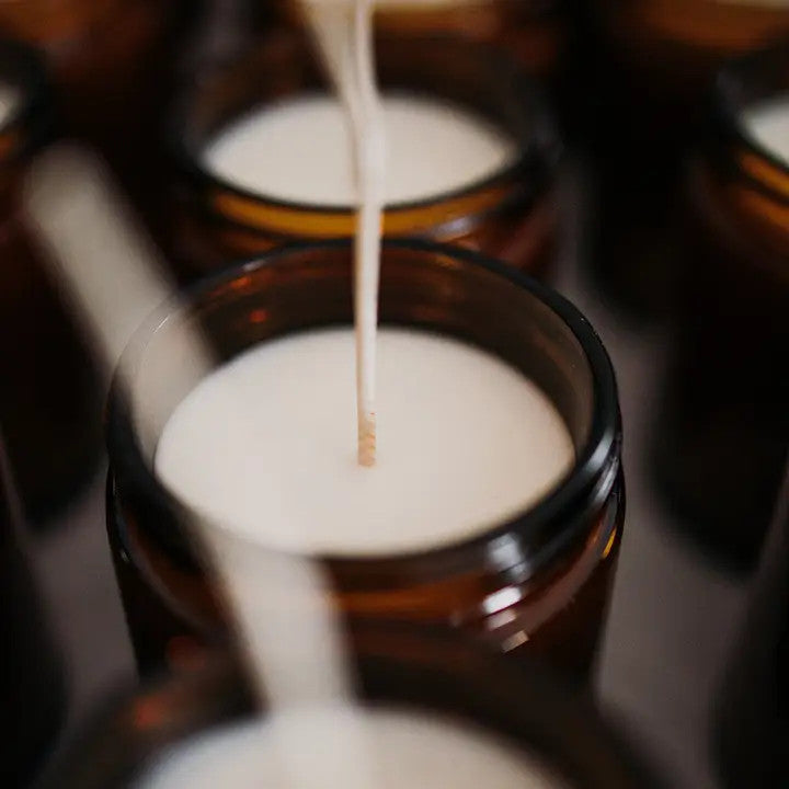 production shot of several candles in their amber glass jars with the lids off revealing the white soy wax and long wicks prior to being cut