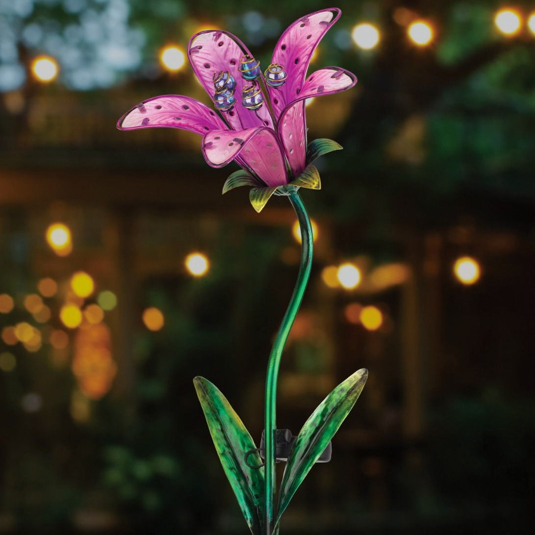 the pink tiger lily solar stake illuminated in a garden at night