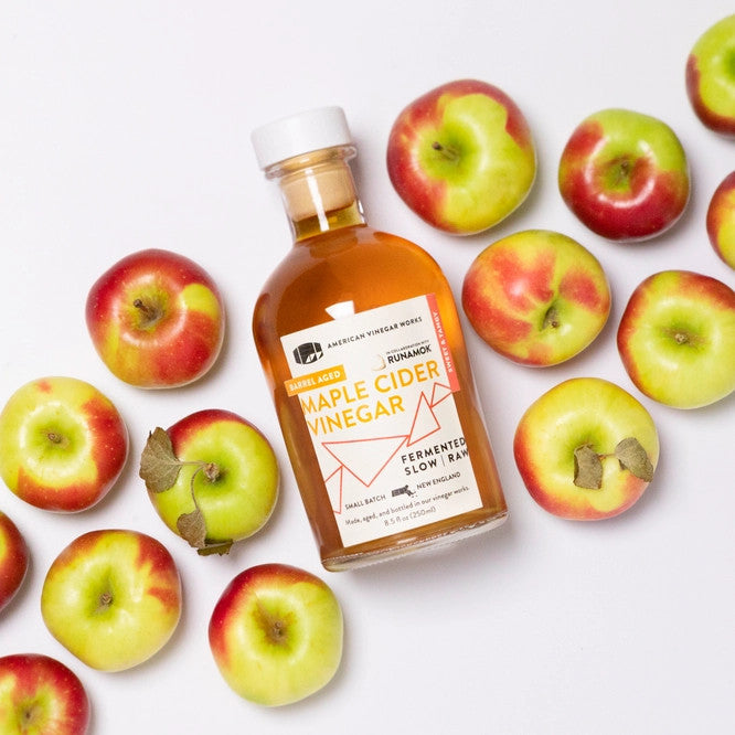 Maple Cider Vinegar bottle laying flat amidst a sweeping diagonal of apples