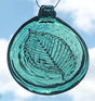 A hand-pressed glass suncatcher with an elm tree leaf pattern, in shades of blue and green, hanging against a sky background.