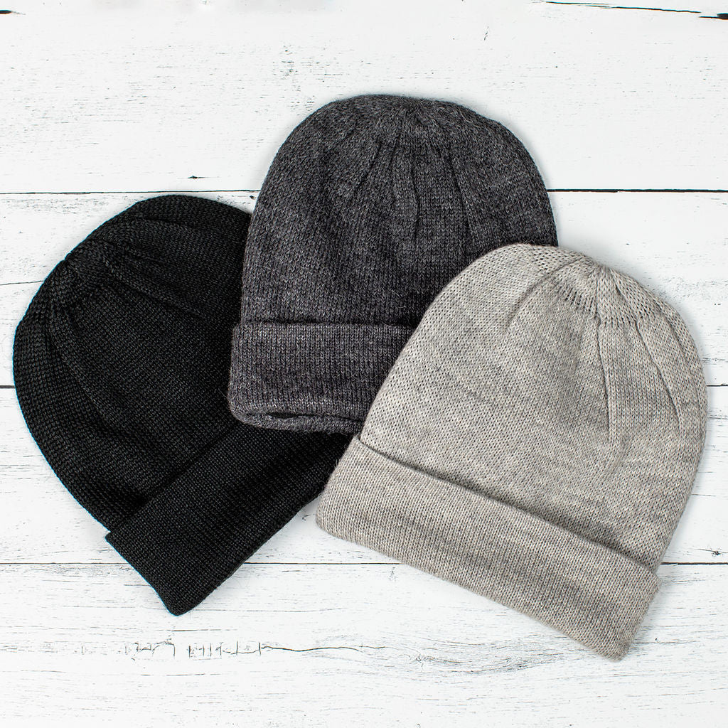 a trio of alpaca hats fanned on a white wood background - colors pictured are black, gray, and silver