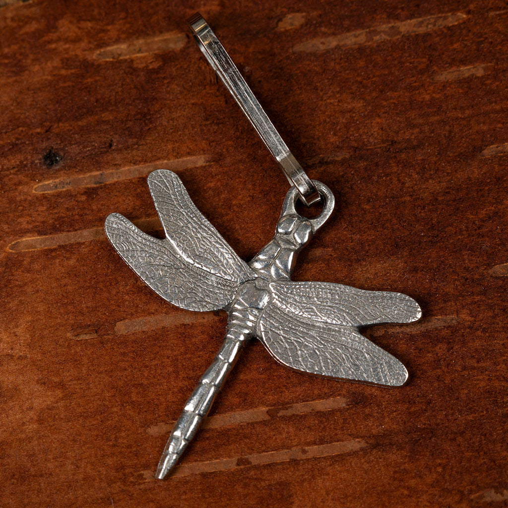 a highly detailed pewter dragonfly zipper pull set against a wood background