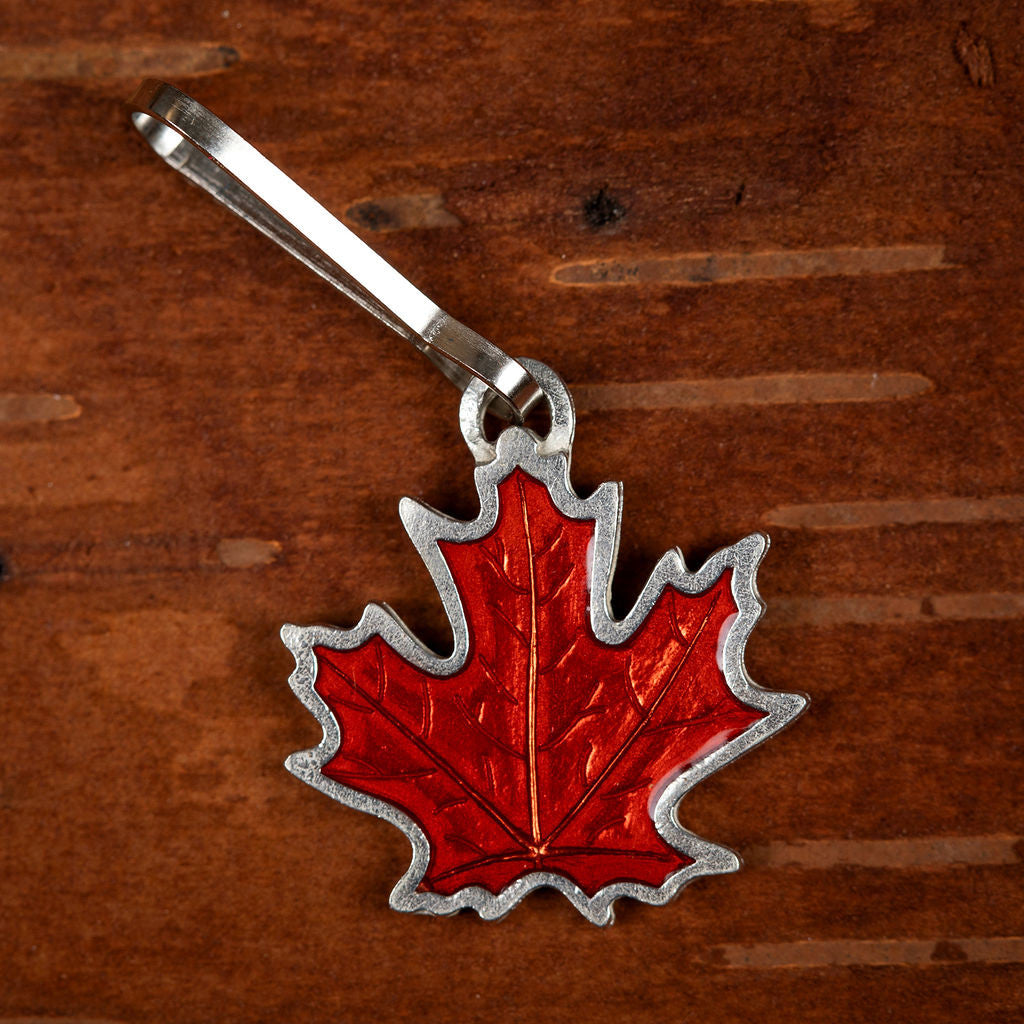 a handcrafted pewter and rust orange colored maple leaf zipper pull on a dark wood background
