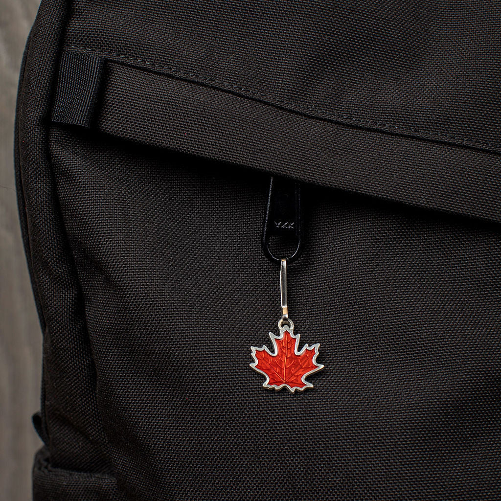 a handcrafted pewter and rust orange colored maple leaf zipper pull on a black backpack