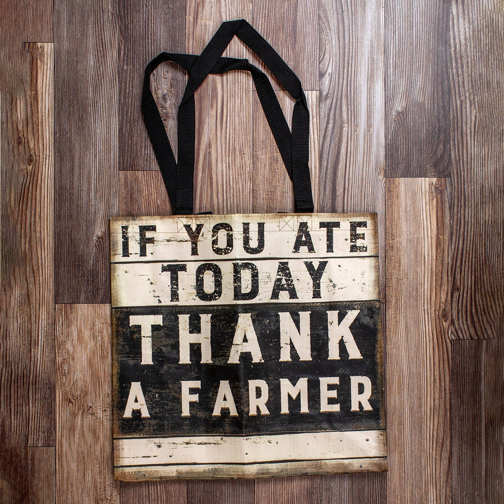 a square woven nylon market tote with wooden plank print and a graphic of black and white painted sign that reads "if you ate today thank a farmer"