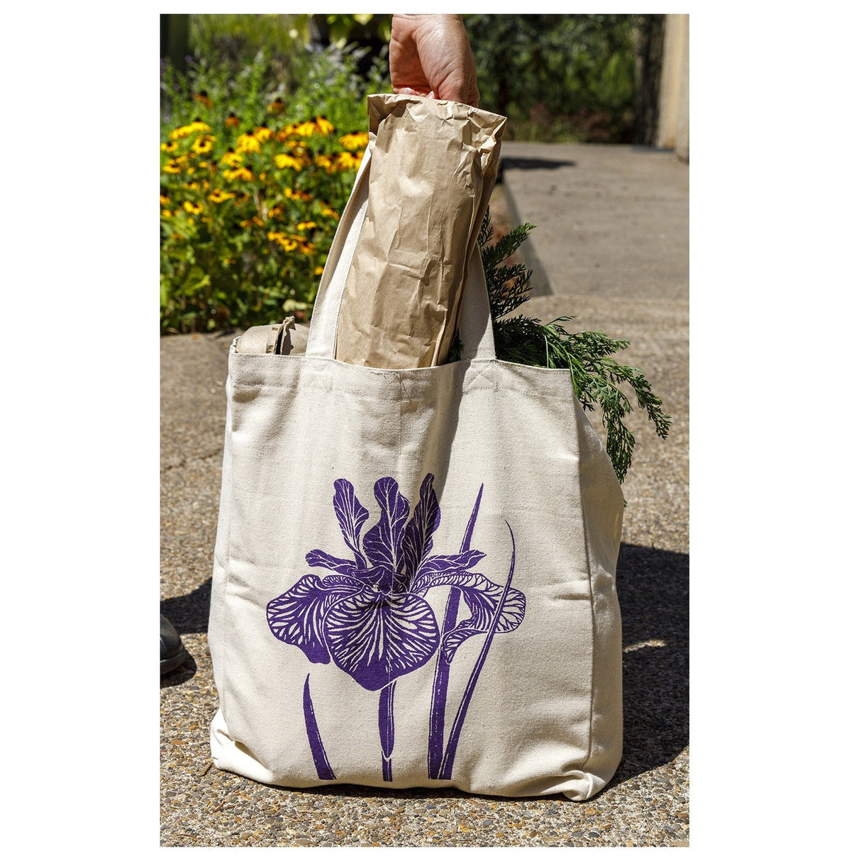 the farmer's market tote outdoors filled with overflowing grocery items with the purple iris side showing