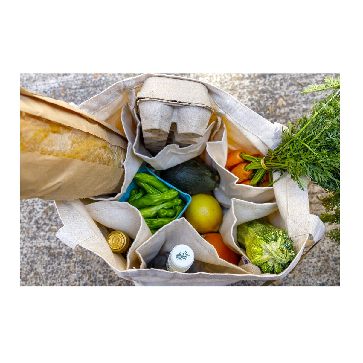 a bounty of groceries viewed from the top of the farmer's market tote bag. More delicate items like eggs and bread are nestled into their own pockets to prevent other items crushing them