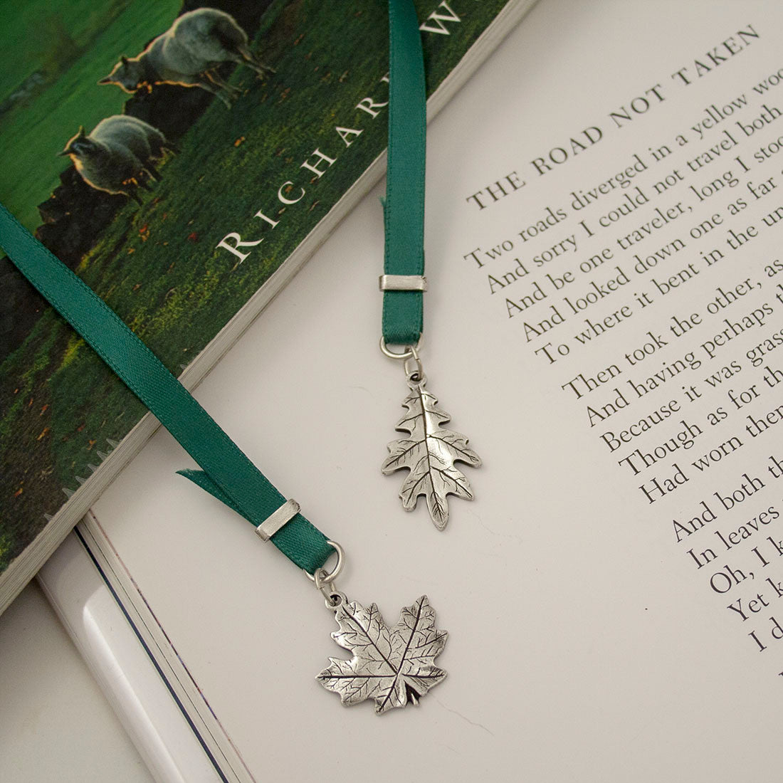 A pewter bookmark in the shape of a leaf attached to a ribbon, resting on an open book.