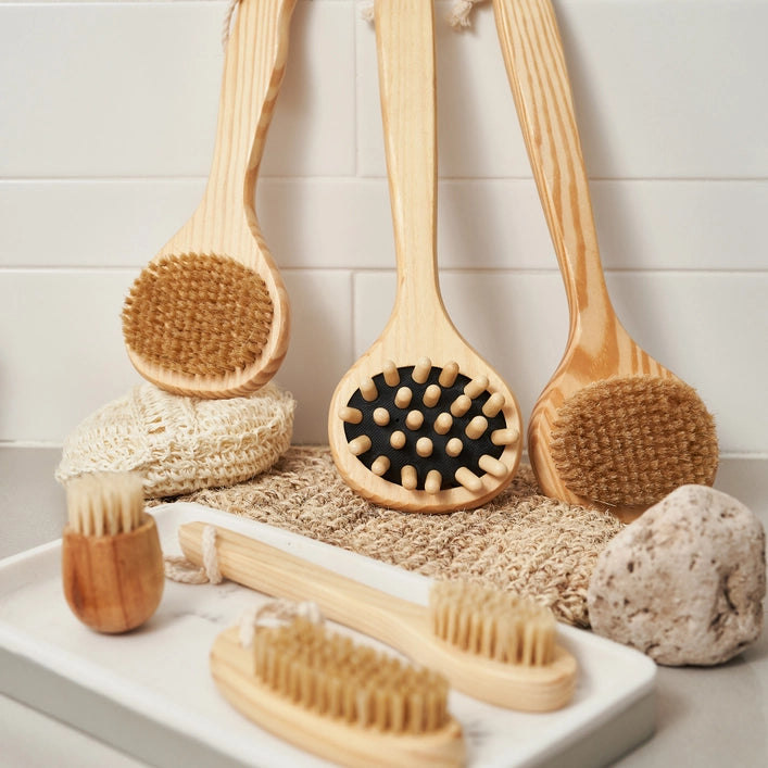 Set of wooden bath brushes and sponges on a white tray with a tiled wall background.
