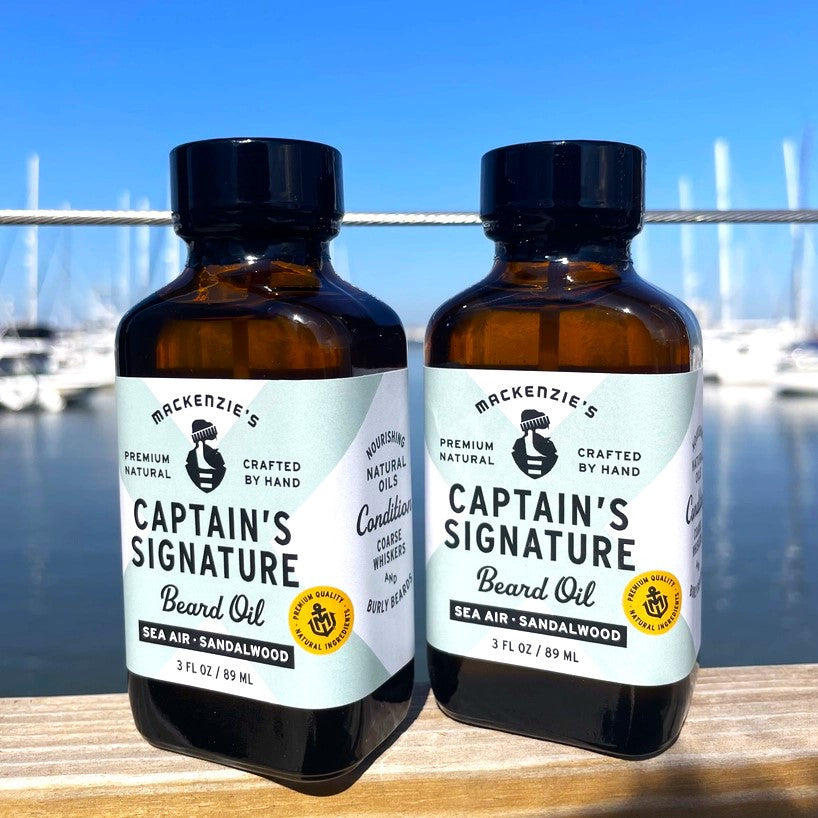 two bottles of the Captain's Signature Beard Oil side by side on a railing overlooking a busy harbor