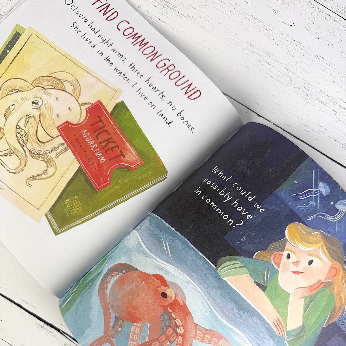 Open children's book with illustrations of an octopus and a girl on a white wooden surface