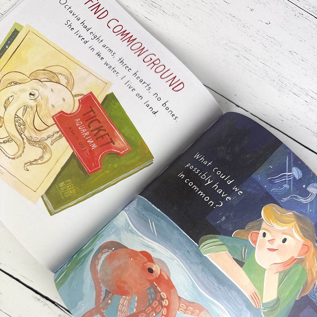 Open children's book with illustrations of an octopus and a girl on a white wooden surface
