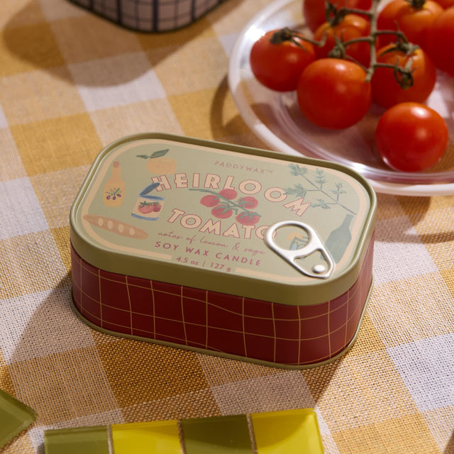 Small tin can with 'Heirloom Tomato' design on a checkered tablecloth with tomatoes in the background.