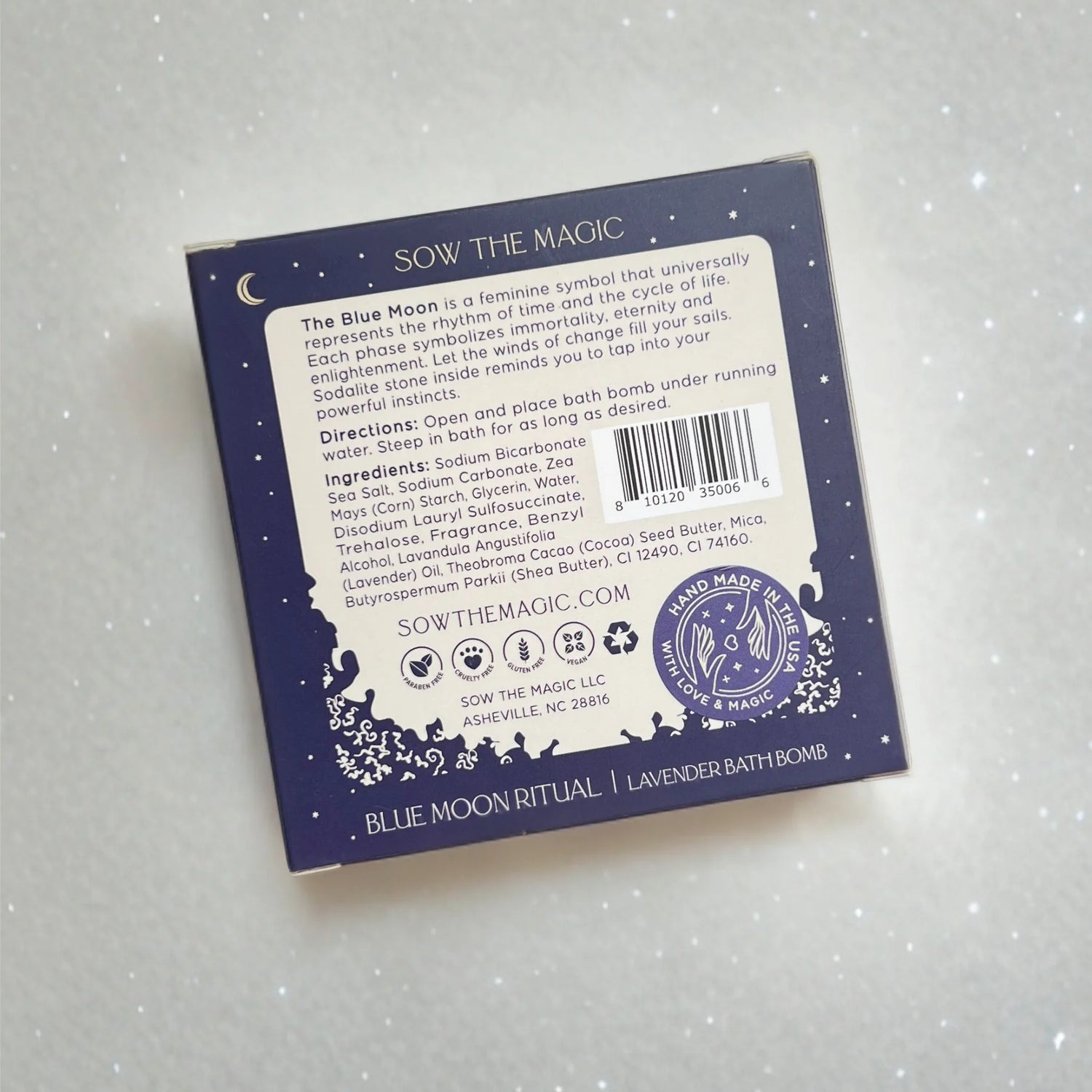 Back of a blue bath bomb packaging with text and branding on a light gray background