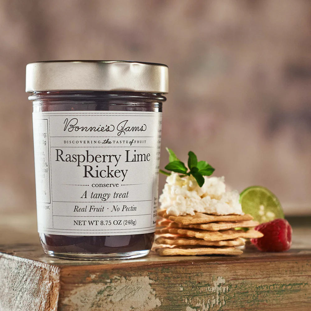 Jar of Raspberry Lime Rickey preserve with crackers and fruit on a wooden surface