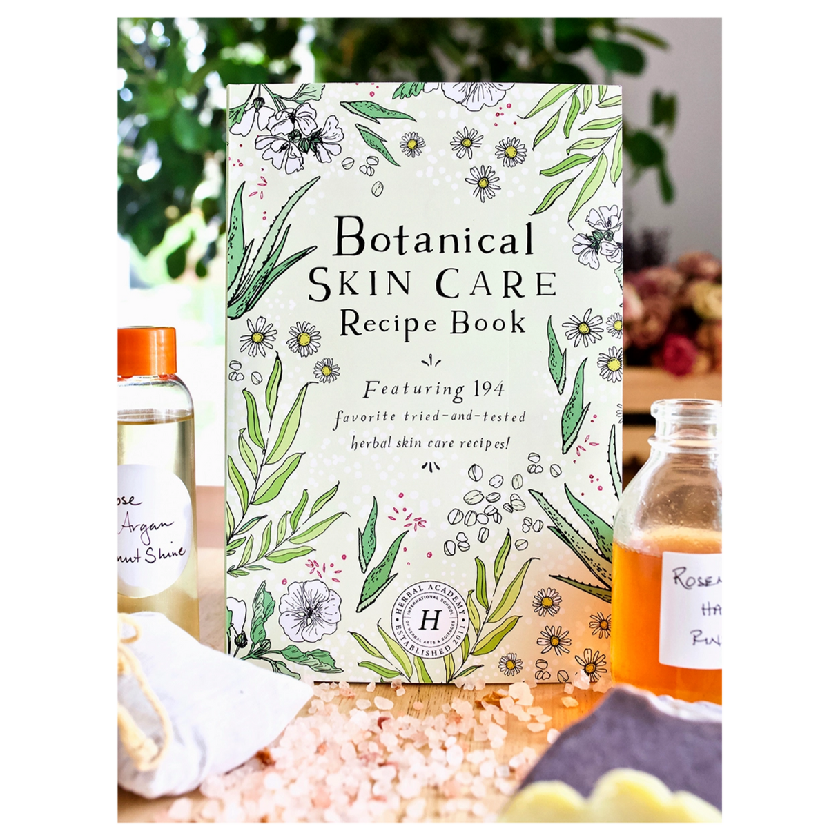 Botanical Skin Care Recipe Book standing on a table surrounded by ingredients and tinctures