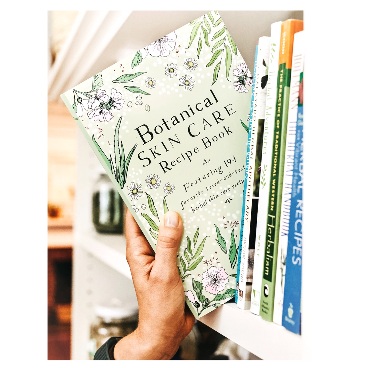 a hand reaching for a copy of the Botanical Skin Care Recipe Book and pulling it from a bookshelf