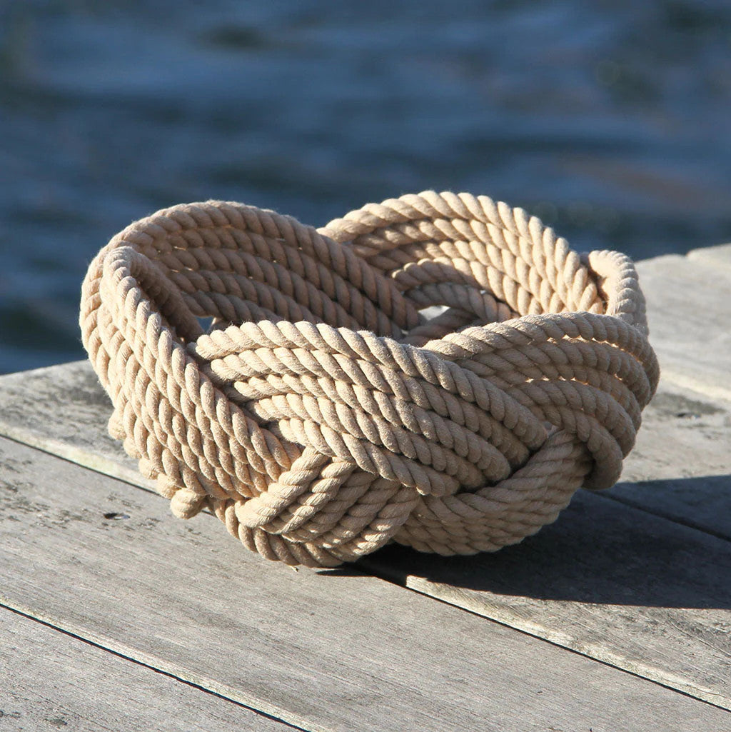 a hand woven cotton rope bowl in tan resting on a dock with a view of the water