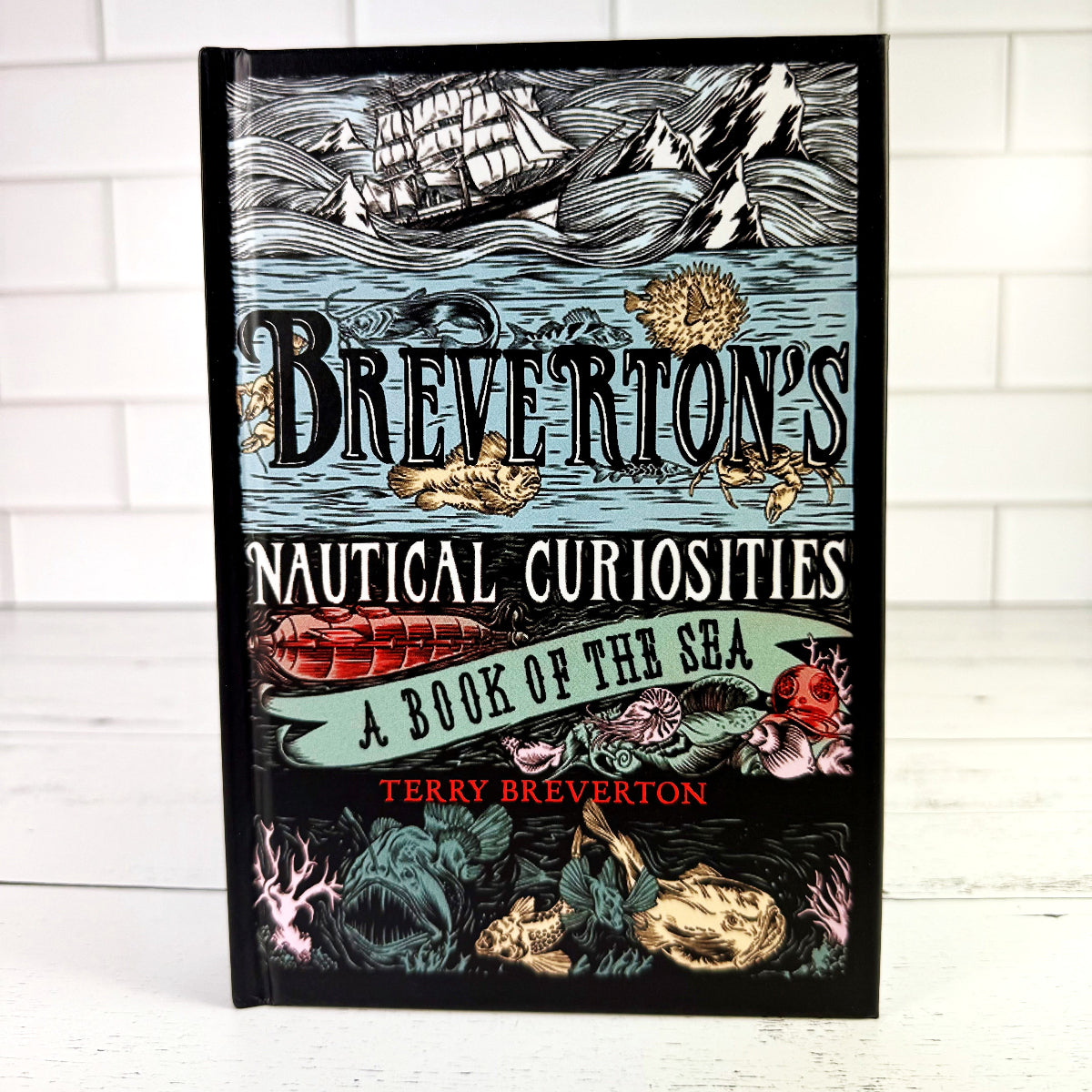 a copy of the book "Breverton's Nautical Curiosities: A Book of the Sea" standing upright on a white wood surface against a white tiled background