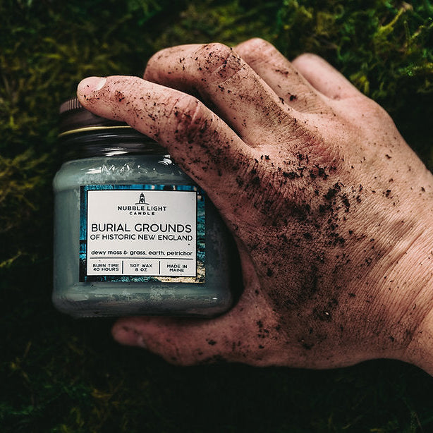 Hand holding a jar labeled 'Burial Grounds of Historic New England' against a grassy background