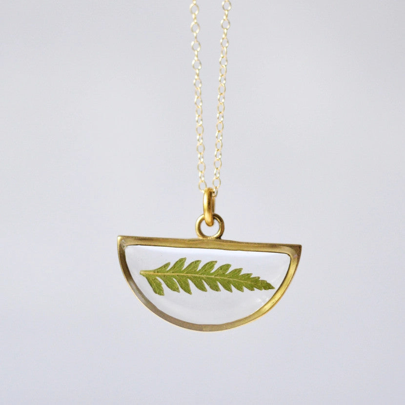 a gold half moon shaped clear resin pendant necklace with real pressed fern inside and outlined in gold, hanging from a gold chain