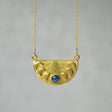 a brass cast pendant features a delicate half moon shape, with each phase of the moon represented in intricate detail. At the center, the full moon is highlighted by crushed lapis lazuli. The pendant hangs from a gold chain