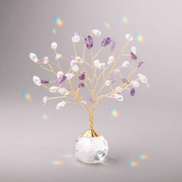 Decorative tree with gold branches and crystal base adorned with amethyst and clear crystals casting tiny rainbows against the light gray background