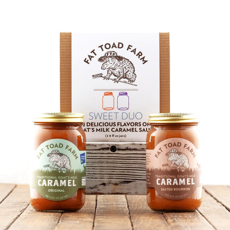 Two jars of Fat Toad Farm caramel sauce with a packaging box in the background on a wooden surface.