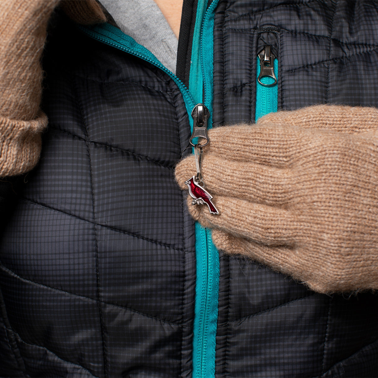 a close up of the cardinal zipper pull on a black coat with a model's gloved hands pulling the zipper pull