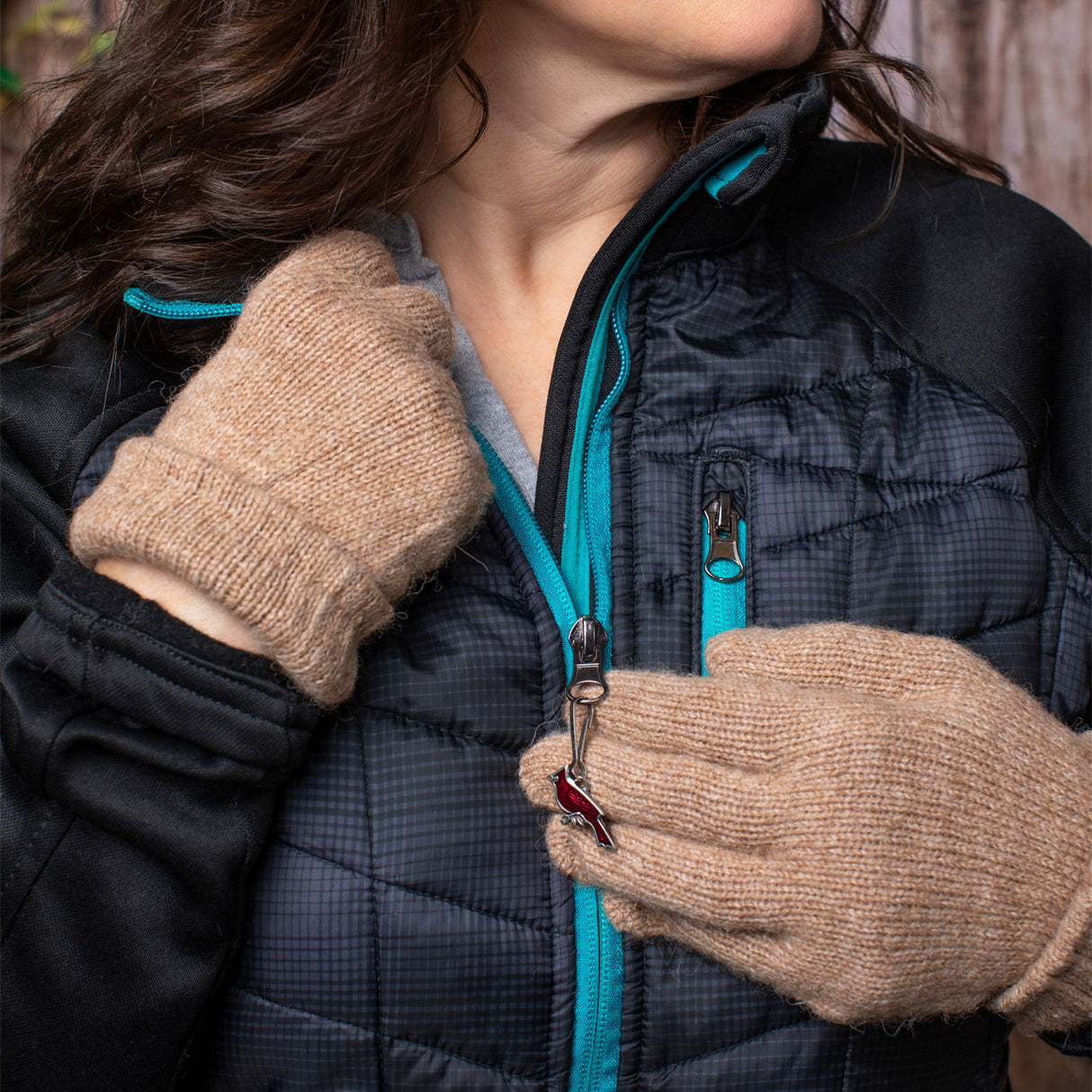 a model wearing a black coat with camel colored gloves unzipping her coat with the cardinal zipper pull resting over her gloves