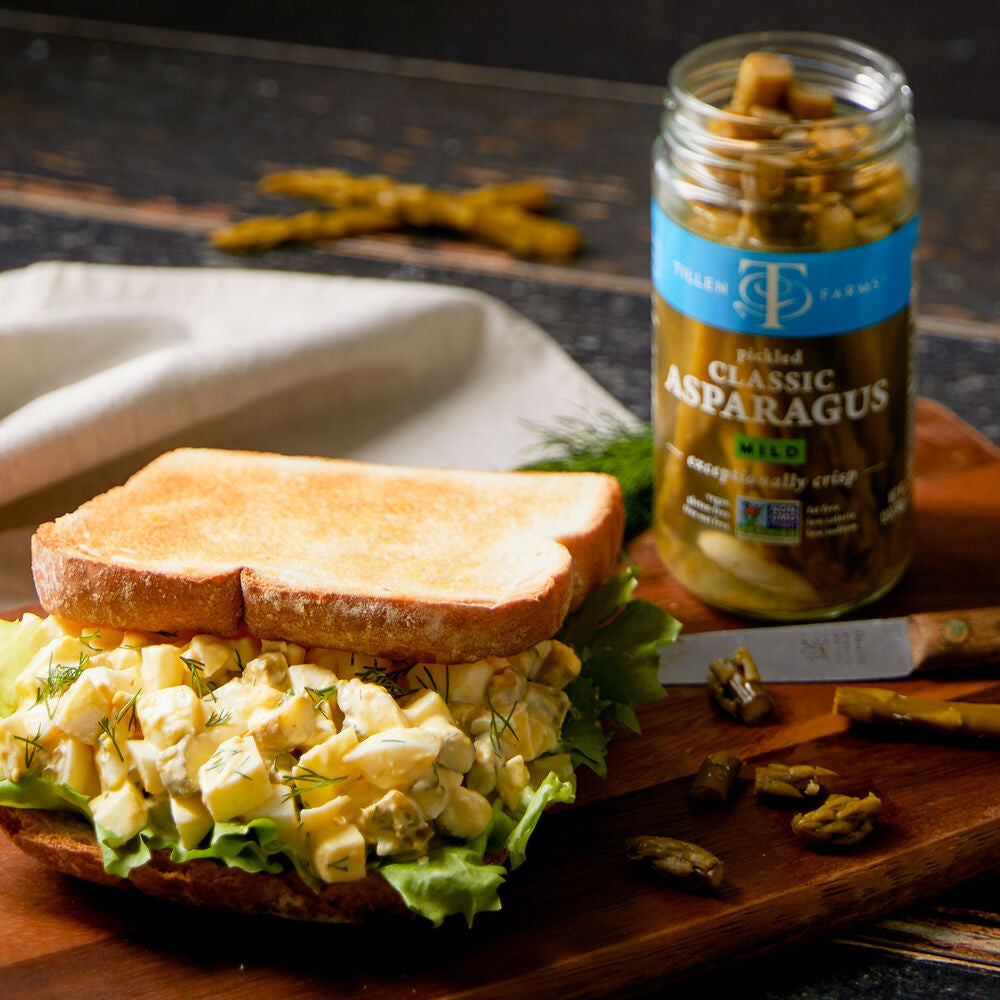 an enticing picknic spread with a sandwich alongside an open jar of pickled asparagus