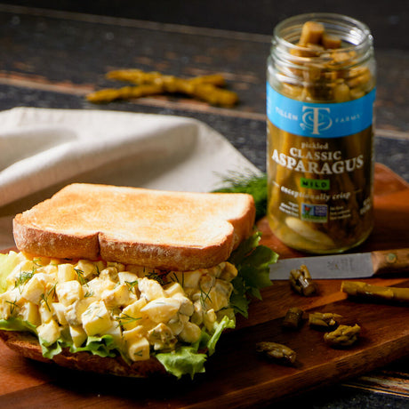 an enticing picknic spread with a sandwich alongside an open jar of pickled asparagus