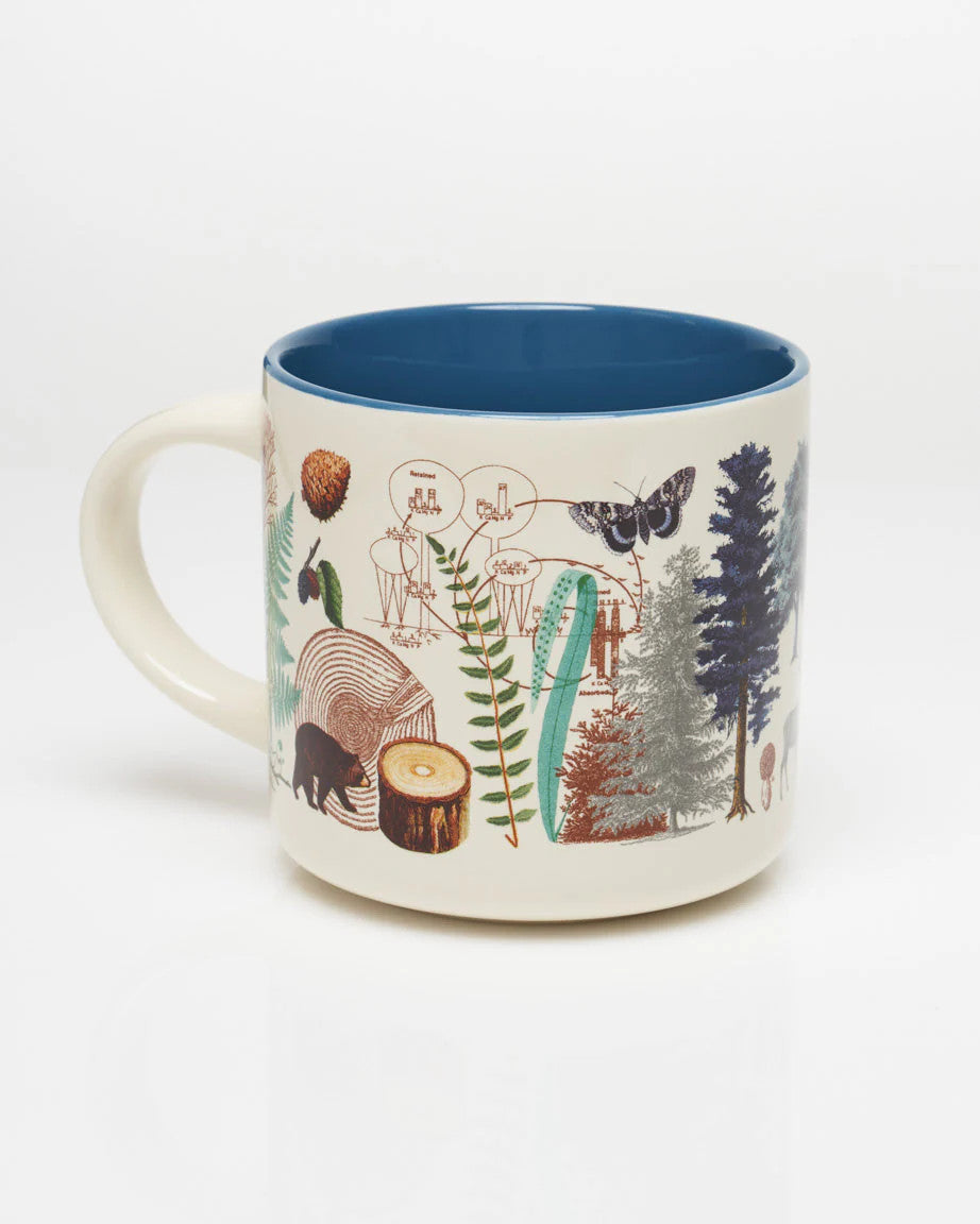 a white coffee mug with vintage illustrations of woodland flora and fauna wrapping around it, and a solid deep blue print on the inside of the mug