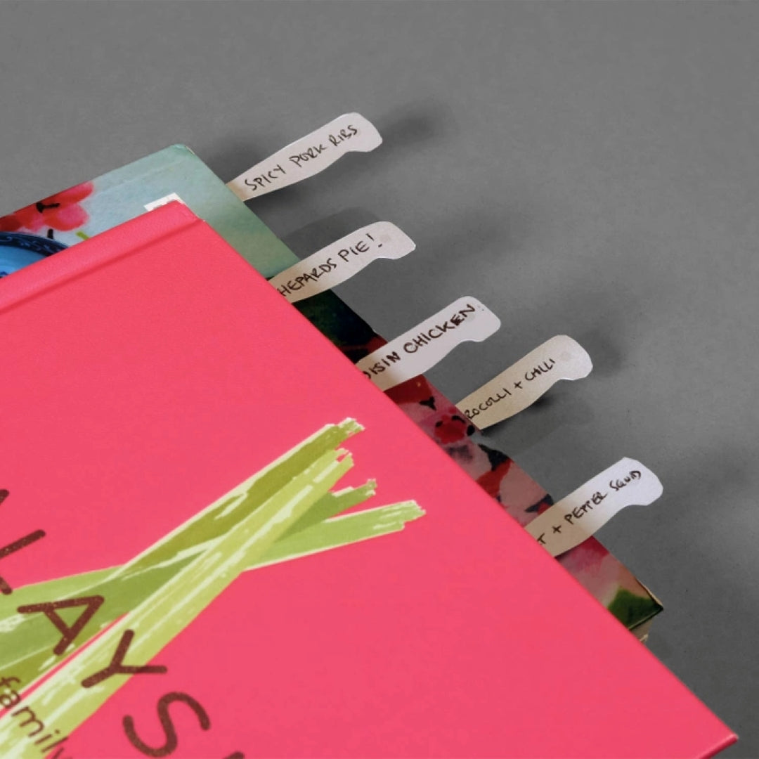 close up of a closed cookbook with cookmarks popping out the top of the book with recipe names written on them