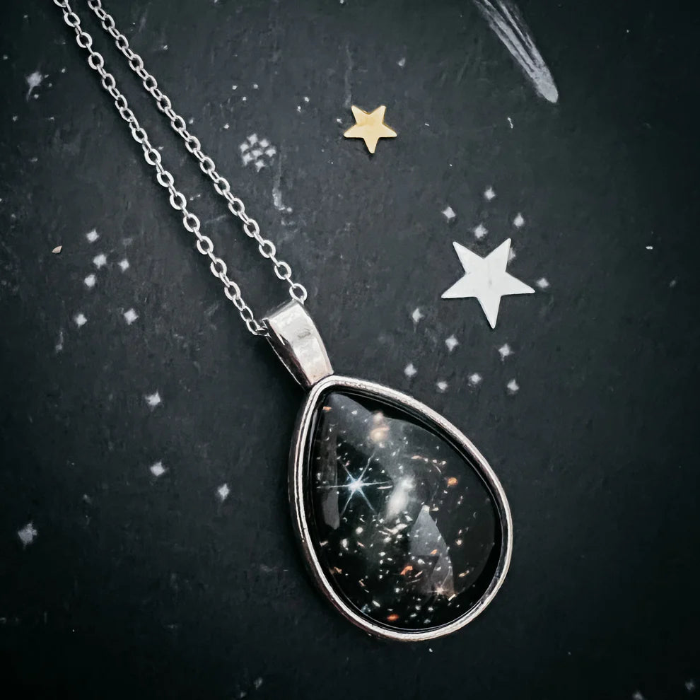 Teardrop-shaped necklace pendant with celestial design on a dark background