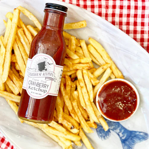 a platter of french fries with a dish filled with cranberry ketchup with the ketchup bottle resting on the pile of french fries all set on a table with red and white checked tablecloth