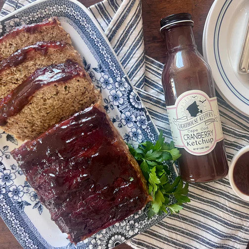 a charming tabletop spread with a sliced meatloaf on a platter that is topped with cranberry ketchup with the bottle of ketchup alongside the platter
