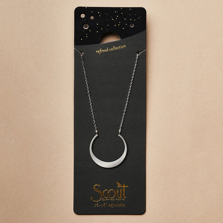 A silver necklace with a crescent moon pendant on a black card that it is packaged with