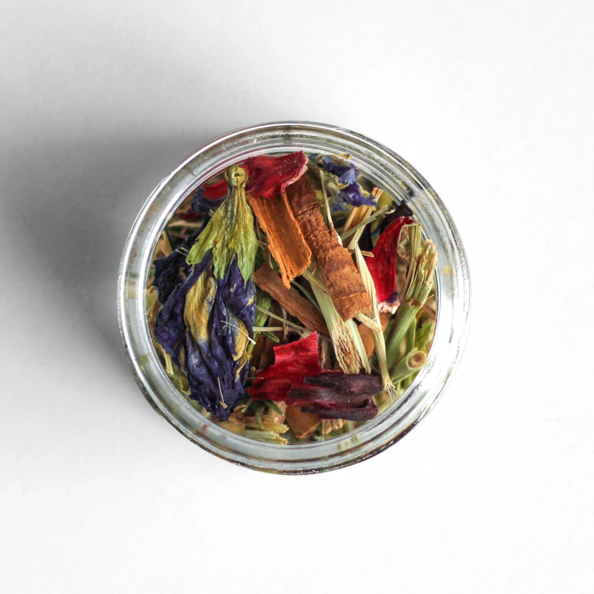 a top down view of a clear glass dish filled with the loose leaf mariposa tea showing the many herbs and purple flowers in the tisane