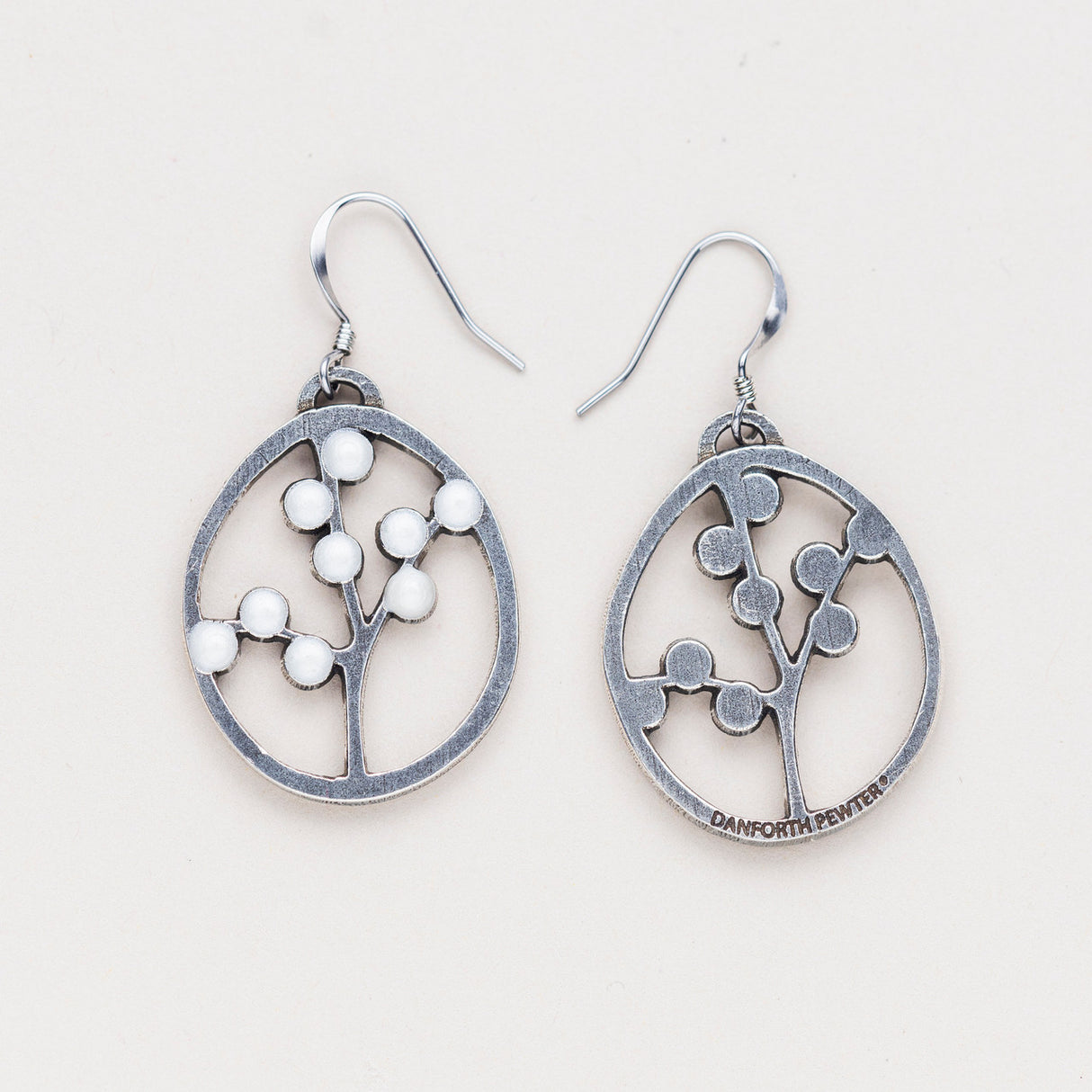 a pair of oval pewter earrings with branches inside adorned with white beads to represent blossoms with one turned over to show the all silver backside with the Danforth Pewter makers mark