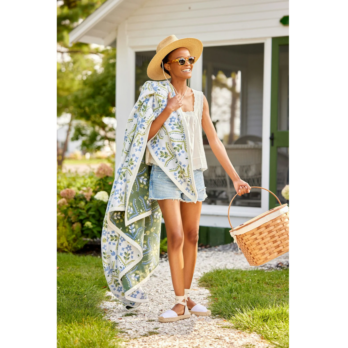 Woman in a garden setting with a floral blanket, straw hat, and sunglasses.