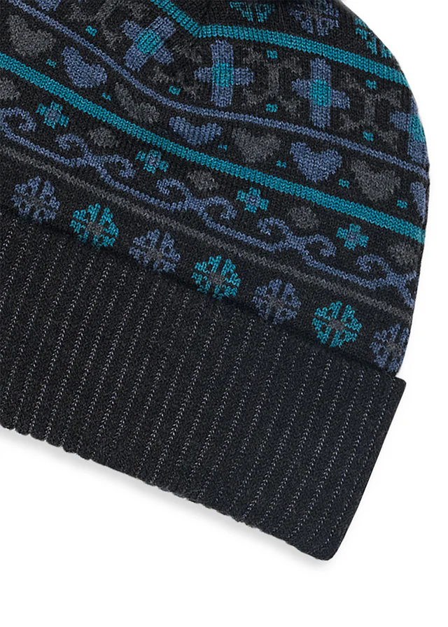 Close-up of a knit beanie with a dark charcoal base, featuring a patterned band in teal, blue, and gray, and a ribbed cuff.