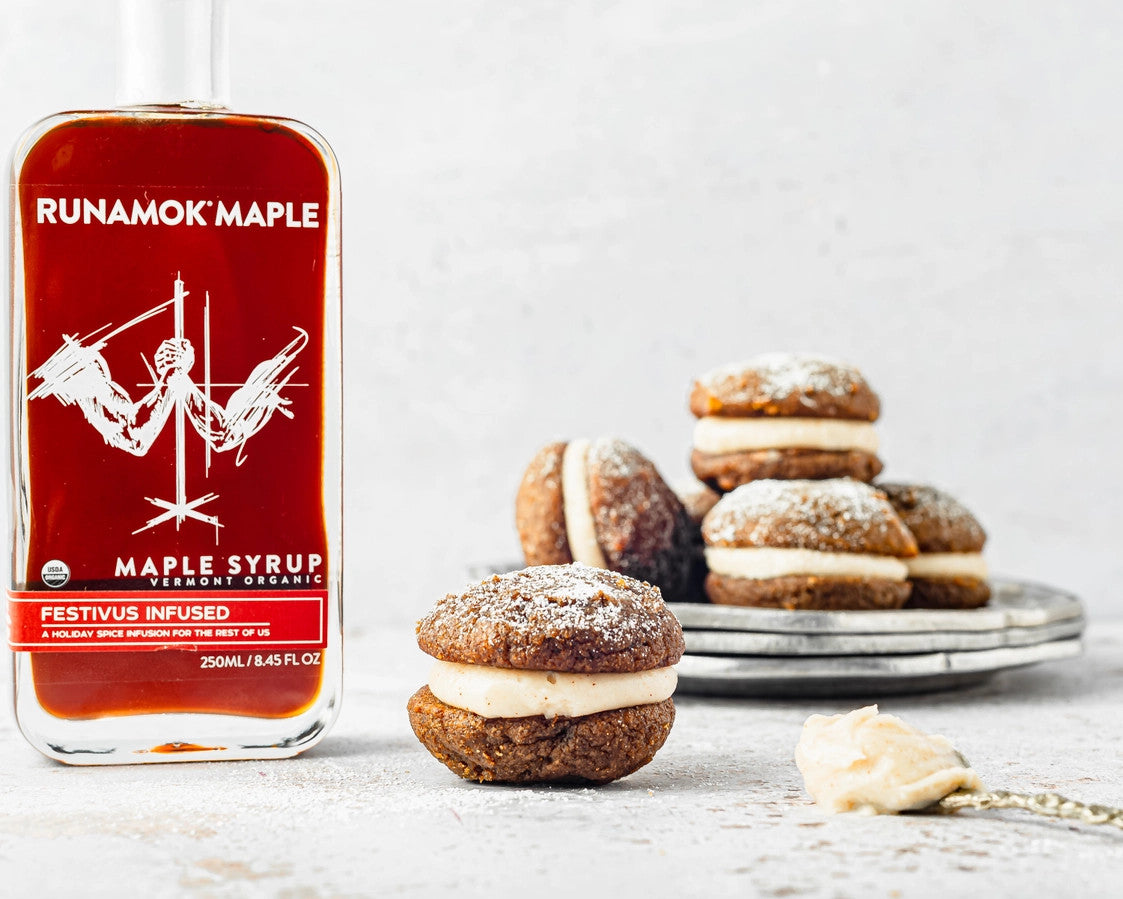 a bottle of festivus infused maple syrup on a countertop next to some gingerbread whoopie pies, highlighting the syrup's potential for use as a baking/flavoring ingredient