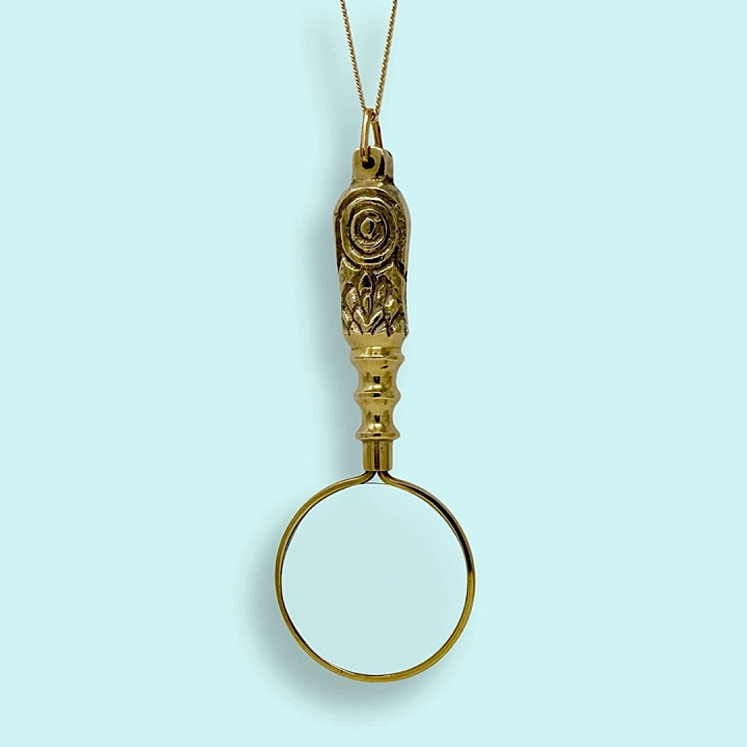 Gold magnifying glass pendant on a light blue background