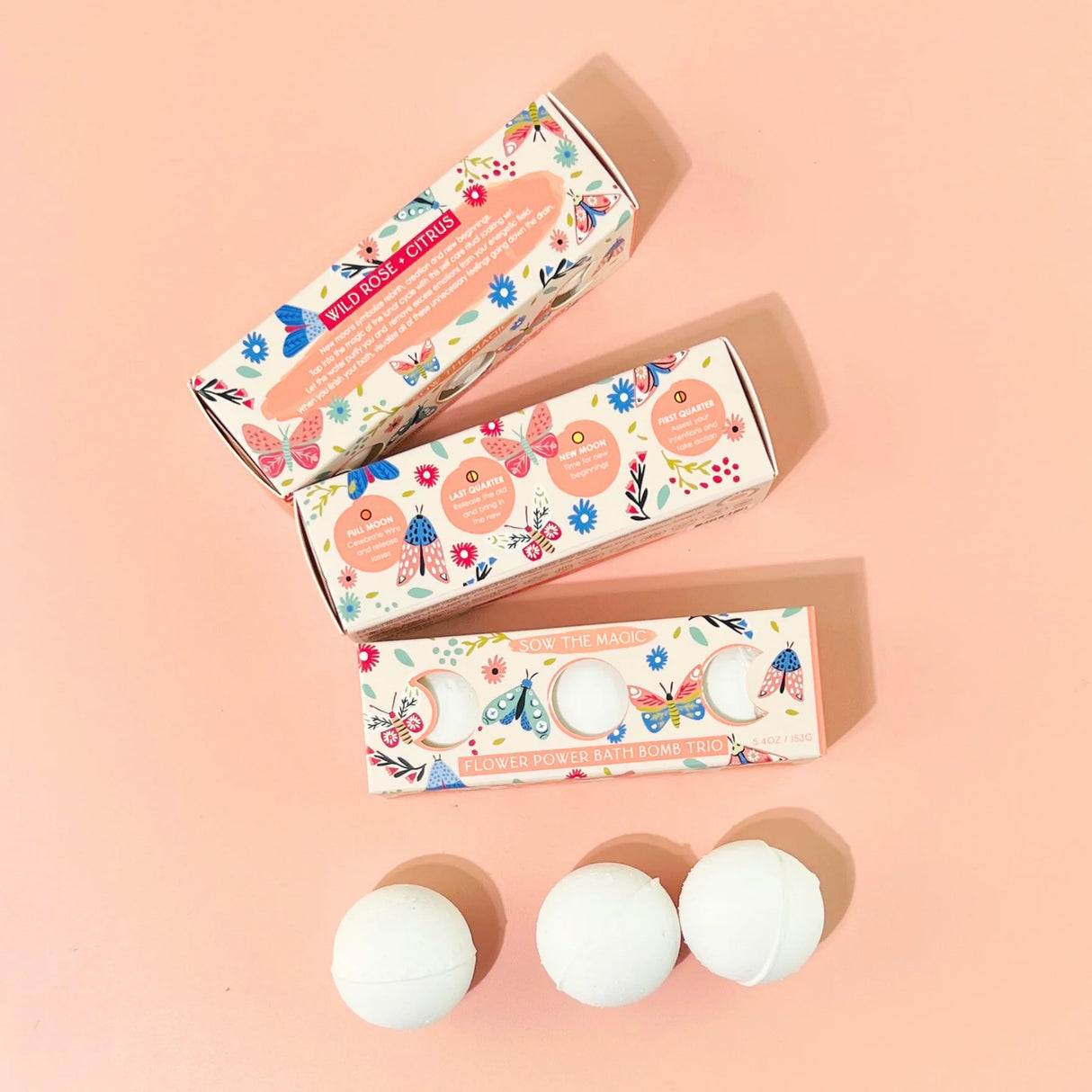 Three white bath bombs with floral packaging on a pink background