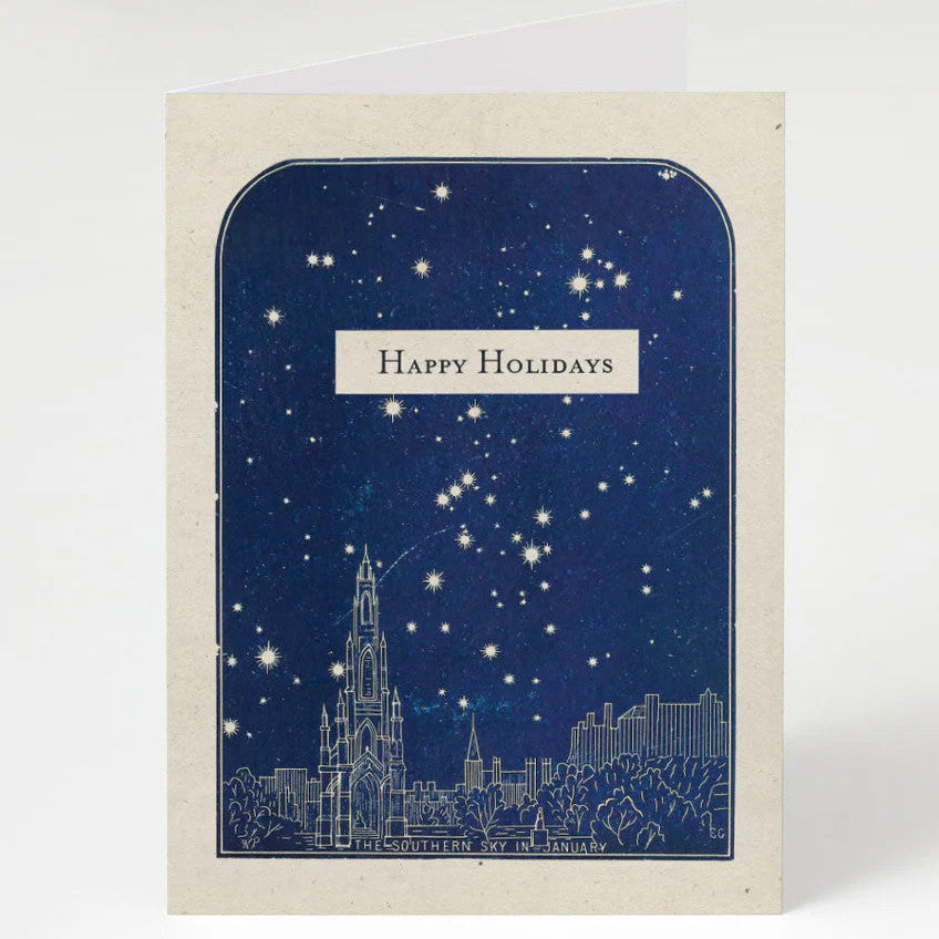 an off white greeting card that reads "Happy Holidays" with a vintage illustration of a city with a navy blue sky of stars shining above it, the bottom of the plate reads "southern sky in january"