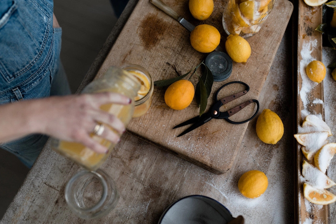 a rustic kitchen counter spread featuring the garden scissors amongst lemons and other tools with someone pouring lemon juice into a glass